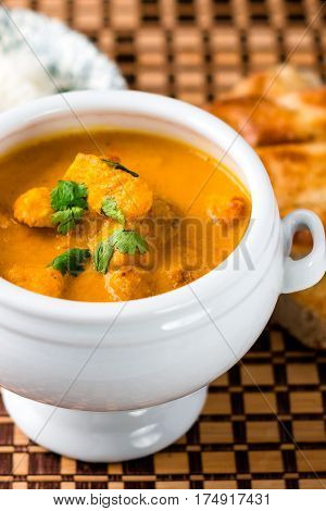 Delicious butter chicken served in a white bowl with naan bread and rice on the side on a wooden place mat.