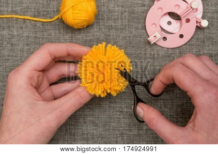 Hands Trimming A Yellow Pom-pom With Thread Scissors