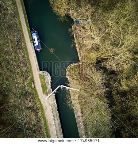 Vertical drone view of an English canal scene with barge lock and towpath surrounded by winter trees on a bright February day.