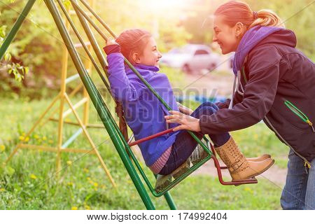 Young Mother Little Daughter on Seesaw in Spring Park Sprtive Casual Clothing Woman and Little Child Outdoor Sunny Day green Grass and shining Sun on Background.