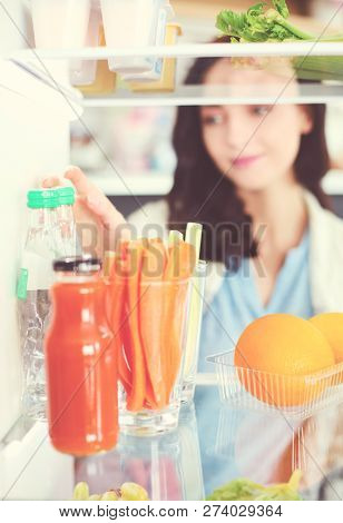 Portrait Of Female Standing Near Open Fridge Full Of Healthy Food, Vegetables And Fruits. Portrait O