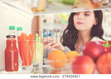 Portrait Of Female Standing Near Open Fridge Full Of Healthy Food, Vegetables And Fruits. Portrait O
