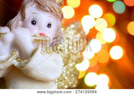 Figurine Of Little Angel With Golden Shiny Wings And Halo That Plays Flute On Shining Background Of 