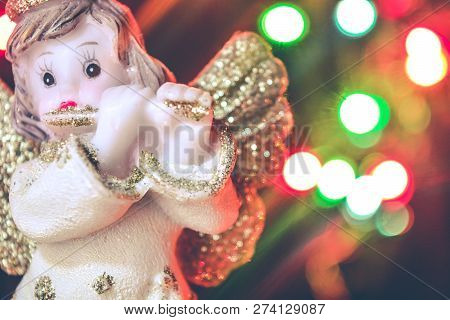 Figurine Of Little Angel With Golden Shiny Wings And Halo That Plays Flute On Shining Background Of 