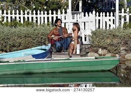 Loving Young Couple Singing And Playing Guitar By A Boat In A Peaceful Stream