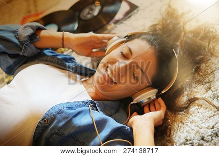 Vibrant young brunette listening to vinyl records with heaphones