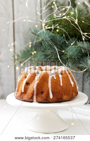 Pie With Raisins And Icing From Powdered Sugar On The Background Of Fir Branches And Garlands. Rusti