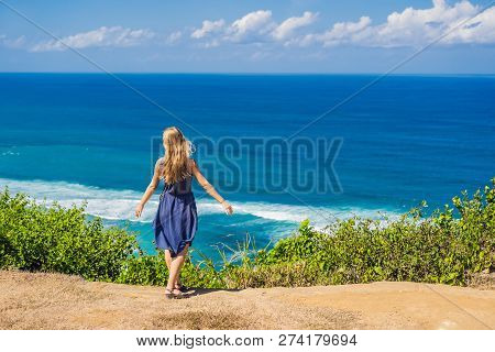 Young Woman Tourist On A Cliff Above The Beach. Empty Paradise Beach, Blue Sea Waves In Bali Island,