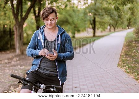 Attractive Young Caucasian Man Taping On The Phone, Sitting On The Bycicle, With White Earrings, In 