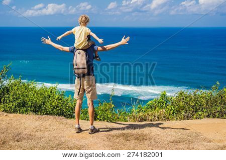 Dad And Son Travelers On A Cliff Above The Beach. Empty Paradise Beach, Blue Sea Waves In Bali Islan