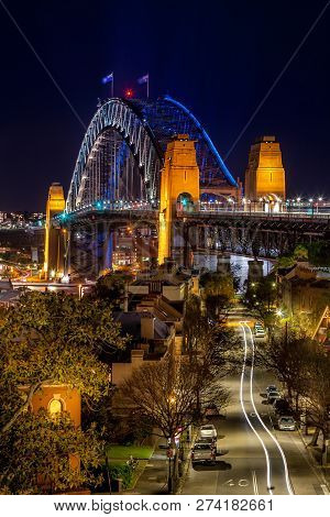 Views Down The Road Towards Sydney Harbour Bridge, Its Arch Lit With Blue And The Light Reflecting I