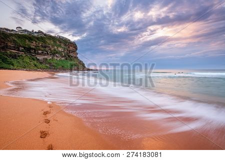 Waves Wash Up Onto Seashore Washing Away Footprints Left In The Sand