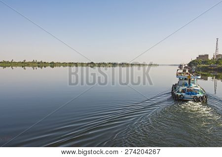 Small Tug Boat Towing A Yacht On Nile River In Egypt Through Rural Countryside Landscape