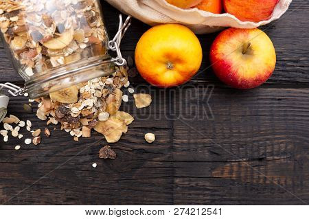 Homemade Granola In Glass Jar And Apples In Reusable Fabric Bag On Dark Wooden Table With Texture. H