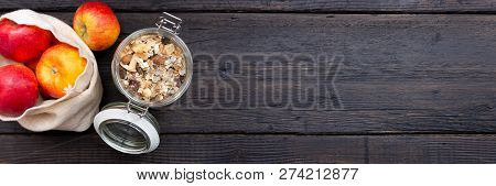 Homemade Granola In Glass Jar And Apples In Reusable Fabric Bag On Dark Wooden Table With Texture. H