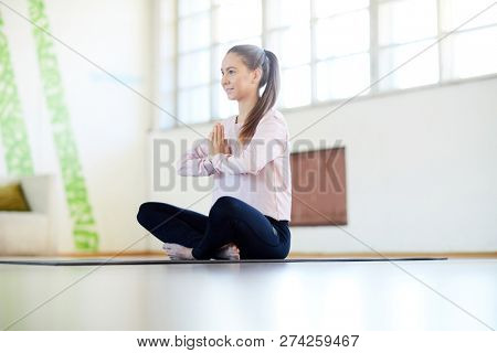 Young active sportswoman sitting on the floor of gy or yoga studio and exercising alone