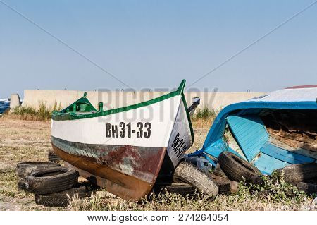 Old Wrecked Rusty Fishing Boat On Dry Grass. Abandoned Ship Stay Far From Water Against Sky. Byala, 