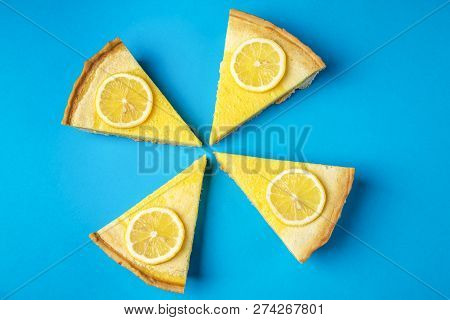 Four Pieces Of Lemon Tart On A Blue Background, Decorated With Yellow Lemon Slices. Home Baked Pastr