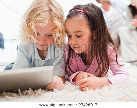 Børn, der bruger en tablet-computer, mens deres forældre er i baggrunden i en stue