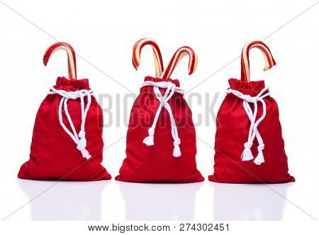 Three red Santa Toy Bags with  a draw string cinching the bags closed as large candy canes protrude out the top.
