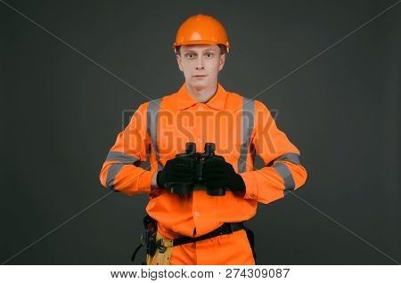 Geodesist Or Builder Foreman With A Binoculars In Hand Isolated On Gray Background.