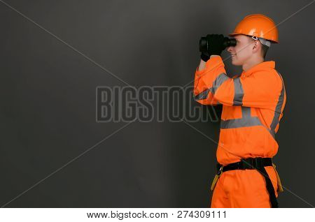 Geodesist Or Builder Foreman Is Looking Through A Binoculars In His Hands Isolated On Gray Backgroun