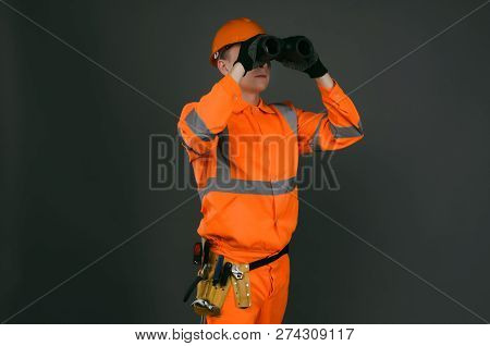 Geodesist Or Builder Foreman Is Looking Through A Binoculars In His Hands Isolated On Gray Backgroun