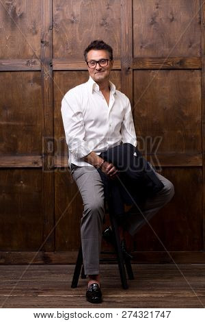 Calm Relaxed Dark Haired Man In White Shirt Smiling And Kindly Looking At You While Sitting On The B