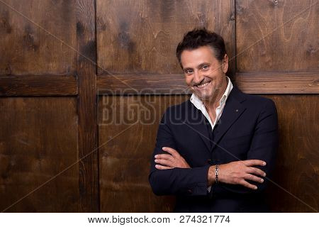 Emotional Relaxed Middle Aged Businessman Smiling While Standing With His Arms Crossed Against The W