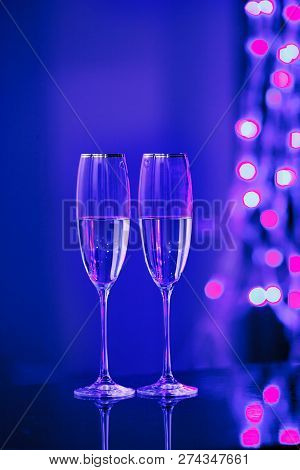 Holiday Pair Of Glasses Of Champagne In The Interior. Blurred Luminocity Neon Color Backdround. Chri