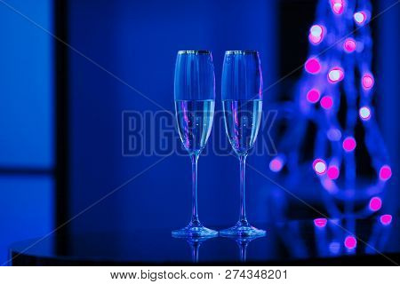 Holiday Pair Of Glasses Of Champagne In The Interior. Blurred Luminocity Neon Color Backdround. Chri