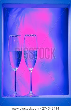 Holiday Pair Of Glasses Of Champagne In The Interior. Blurred Luminocity Neon Color Backdround. Holi