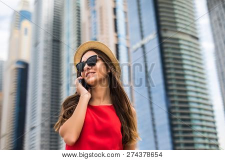 Portrait Of Young Smile Woman In Red Dress, Sunglasses And Summer Hat Talking On The Phone On Downto