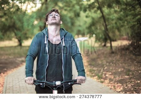 Romantic Young Caucasian Handsome Male With Curly Hair Looks Up Bicycling Alone Through The Green Pa