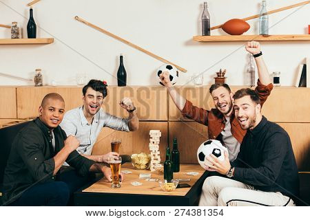 Happy Multicultural Friends Gesturing While Sitting At Tabletop With Beer And Snacks In Cafe
