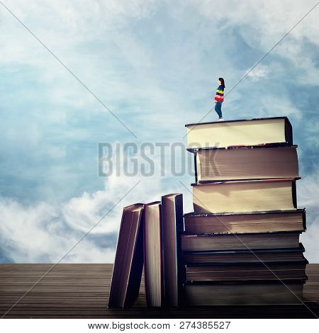 Surreal View As Young Woman Student Stand On The Top Of A Huge Pile Of Books Looking Far At Horizon 