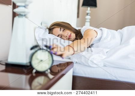 Sleepy Young Woman Stretching Hand To Ringing Alarm To Turn It Off. Early Wake Up, Not Getting Enoug