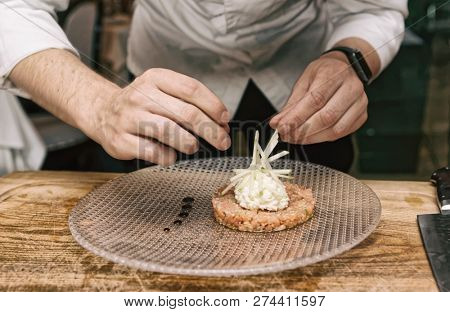 Chef is decorating salmon tartar with cut apple and whipped cheese cream, toned image
