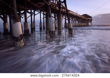 Waves Of The Atlantic Ocean Flow Between The Pylons Of Cocoa Beach Pier In Florida At Daybreak