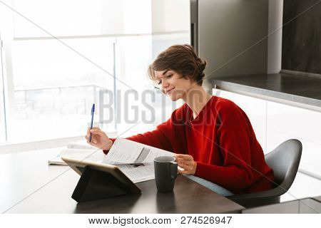 Smiling pretty young woman studying with a tablet computer at the table on a kitchen at home