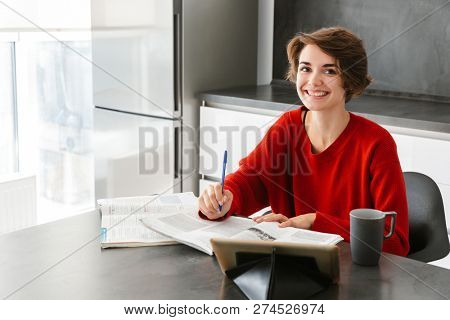 Smiling pretty young woman studying with a tablet computer at the table on a kitchen at home