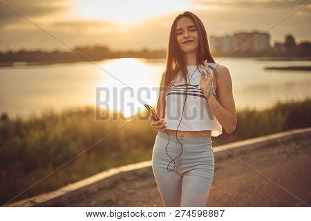 Young Beautiful Caucasian Girl Listening To Music With Smartphone Walking In The City With Headphone