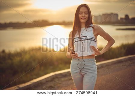 Young Beautiful Caucasian Girl Listening To Music With Smartphone Walking In The City With Headphone