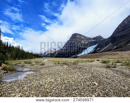 An Open Valley Of Rocks And Creeks Leading Towards The Teal Waters Of Berg Lake And Mount Robson Gla