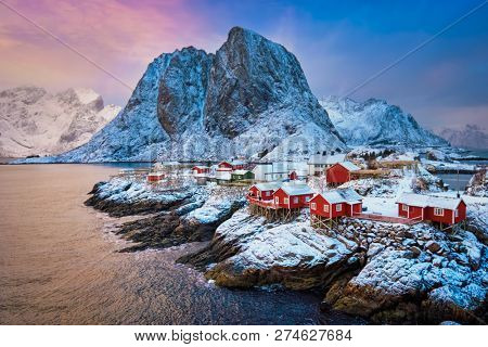 Famous tourist attraction Hamnoy fishing village on Lofoten Islands, Norway with red rorbu houses. With falling snow in winter on sunrise