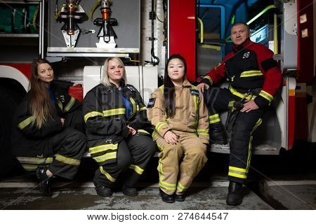 Photo of three firewomen,fireman on background of fire truck