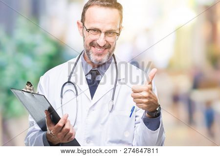Middle age senior hoary doctor man holding clipboard over isolated background happy with big smile doing ok sign, thumb up with fingers, excellent sign