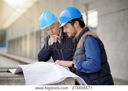 Workmen in hard hats consulting over blueprint on modern building sight