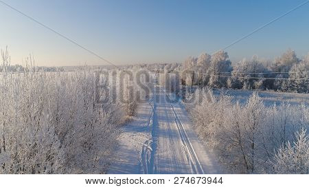 Aerial View Winter Landscape Countryside Road Through Winter Field With Forest. Winter Forest On Sun