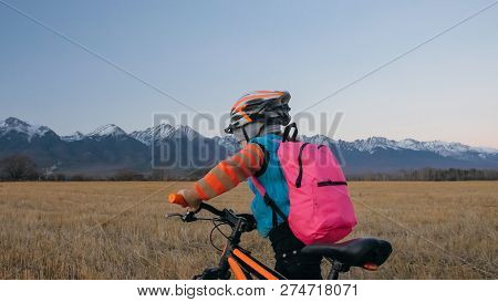 One Caucasian Children Walk With Bike In Wheat Field. Little Girl Walking Black Orange Cycle On Back
